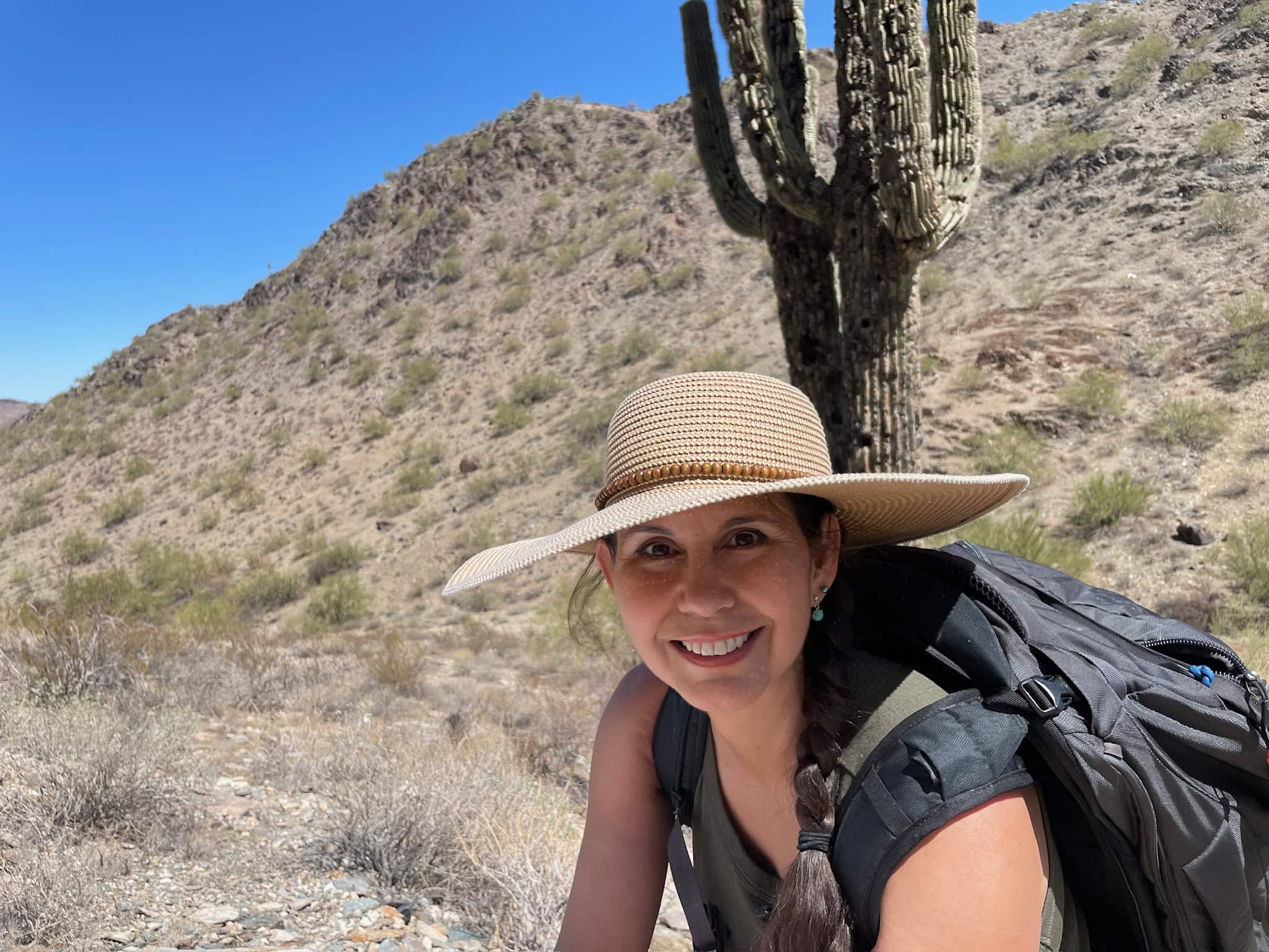 Michelle Gaylor wearing a backpack and sun hat with saguaro cactus and mountain in the background
