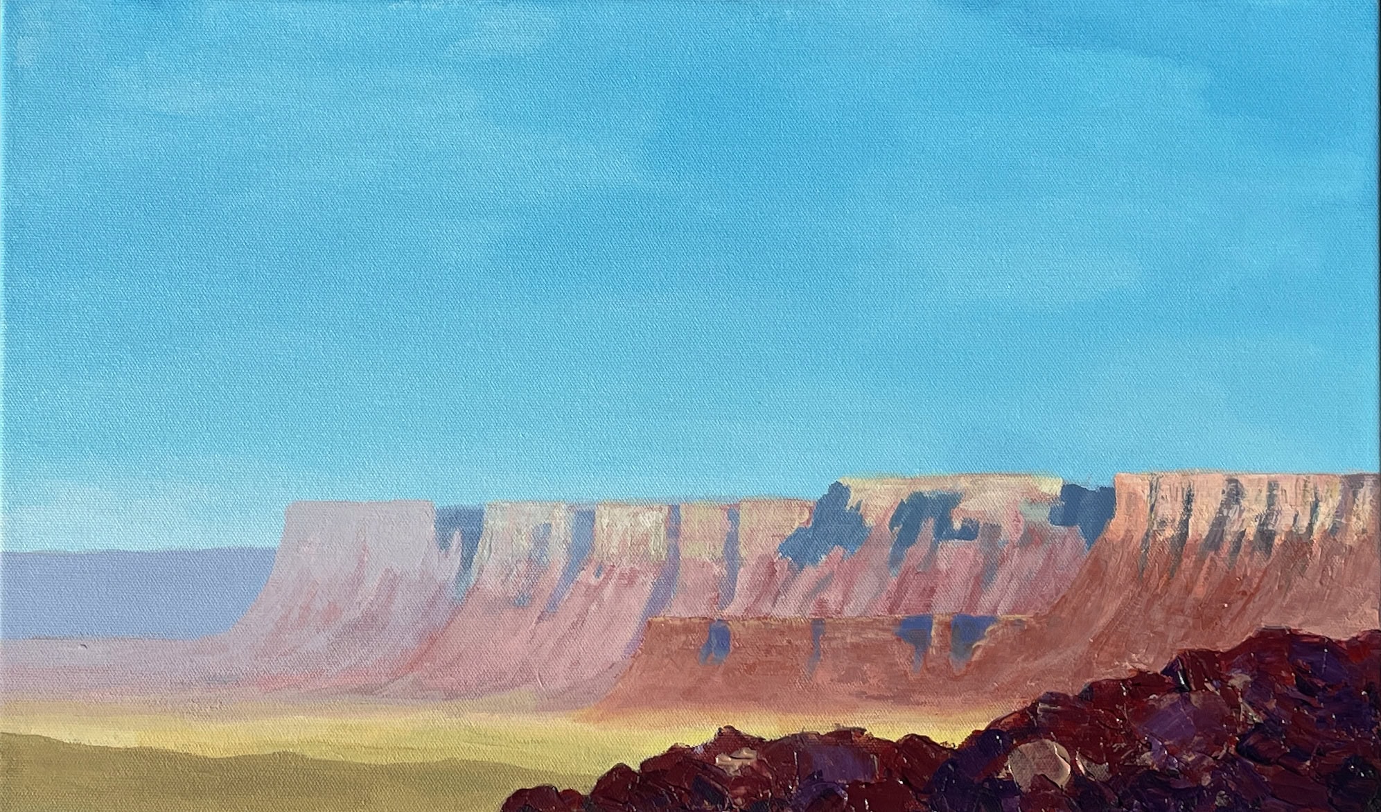 Distant ridge of cliffs forming the edge of a mesa across open desert with a ridge of rocks in the foreground